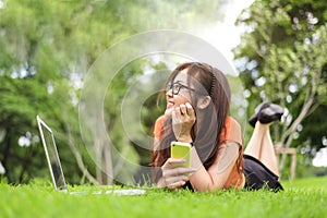 Happy Asian woman resting and looking beside in park with smartphone. People and lifestyles concept. Technology and Beauty theme