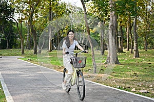 Happy Asian woman riding a bicycle in the park on the weekend, enjoys doing outdoor activity