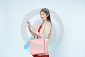 Happy Asian woman with shopping bags in hand is using her smart phone for online shopping while isolated on white background