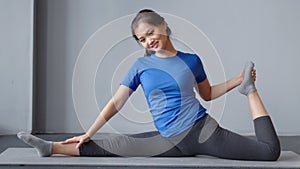 Happy Asian woman showing amazing stretching at pilates class sitting on mat full shot