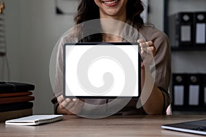 Happy asian woman showing tablet computer with blank screen while sitting at office, mockup for advertising.