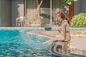 Happy asian woman sitting by pool side having goodtime on summer vacation in hotel and resort