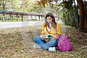 Happy Asian woman sitting and reading books in university park under big tree. People lifestyles and education concept. Summer