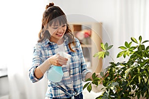 Happy asian woman spraying houseplant at home