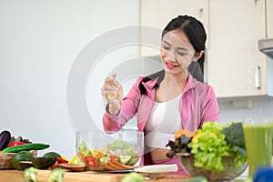 A happy Asian woman is squeezing a lemon on her salad, making her healthy breakfast in the kitchen