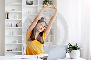 Happy asian woman stretching with her arms raised, taking break at her home office