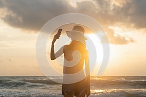 Happy Asian woman taking a selfie to post on social media at beach during travel holidays vacation outdoors at ocean or nature sea