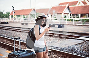 Happy asian woman tourist using cell phone and waiting train at train station,Travel and vacation concept