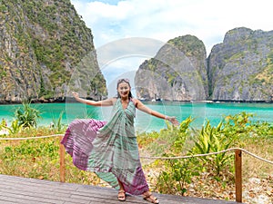 Happy Asian woman tourist at wooden terrace viewpoint with a beautiful landscape of Maya bay beach at Phi Phi Leh islands