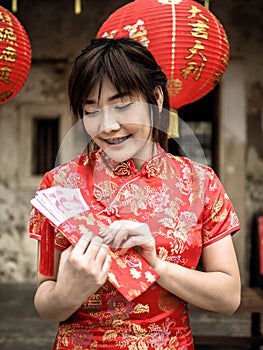 Happy asian woman in traditional chinese dress holding a red pocket with Chinese one hundred Yuan banknotes- lucky money. Tet