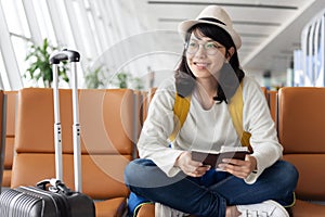 Happy Asian woman traveler is waiting for the flight at the airport