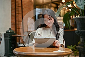 A happy Asian woman is using her tablet while relaxing at a beautiful coffee shop in the city