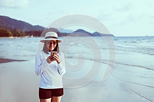 Happy asian woman using mobilephone on the beach near sea while beautiful sunset time,Relaxing and enjoying concept
