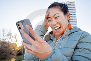 Happy asian woman using the smart phone outdoors. Real people and technology concept.