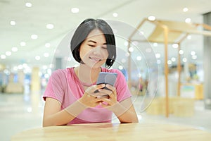 Happy Asian woman using smartphone on table at department store