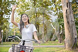 Happy Asian woman waving hand, say hello to her friends while riding a bike in the public park