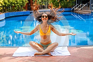 A happy asian woman wearing a bikini and relaxing on the side of a swimming pool.