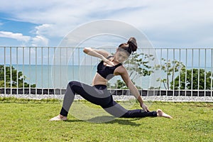 Happy Asian woman wearing black sport wear relaxing in yoga High Lunge twist pose with beautiful sea view