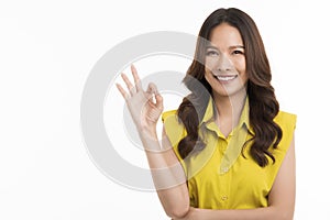 Happy Asian woman wearing a green shirt shows the ok sign and looks at the camera on white background