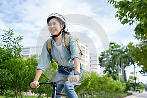 Happy Asian woman wearing a helmet and listening to her favorite music while riding a bicycle through a city park