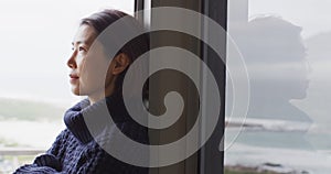 Happy asian woman wearing pullover relaxing and thinking at window alone