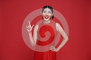 Happy Asian woman wearing red dress with hands pointing finger to copy space isolated on red background