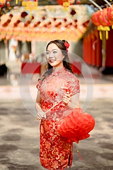 Happy Asian woman wearing traditional cheongsam qipao dress looking confident holding lantern in Chinese Buddhist temple.