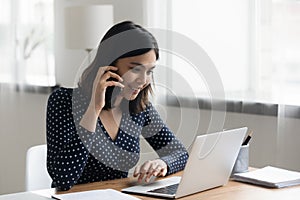 Happy asian woman work on laptop talking on cell