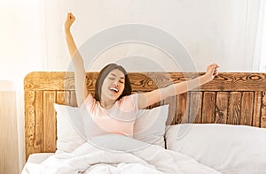 Happy asian woman yawning waking up in bed at home