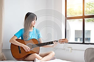 Happy asian women enjoy singing by playing guitar while sitting on sofa at home