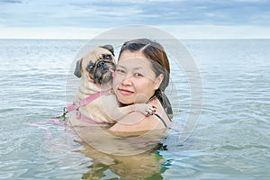 Happy Asian women girl hug play immersed in beach sea water with cute dog puppy pug