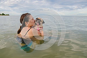 Happy Asian women girl hug play immersed in beach sea water with cute dog puppy pug with kiss in weekend holiday