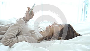 Happy Asian women are using smart phone on the bed in morning. Asian woman in bed checking social apps with smartphone.