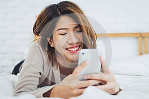 Happy Asian women are using smart phone on the bed in morning. Asian woman in bed checking social apps with smartphone.