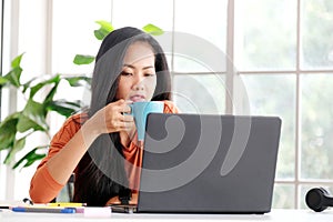 Happy asian women working online with laptop computer at home office, Asia female smiling and holding coffee cup while relaxing