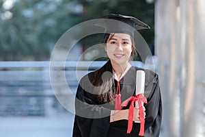 Happy Asian young beautiful graduate female student with University degree standing and holding diploma in hand after graduation