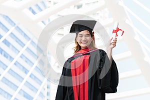 Happy Asian young beautiful graduate female student with University degree standing and holding diploma in raised hand