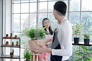 Happy Asian young couple in apron smiling at each other as they look after plants in greenhouse at home