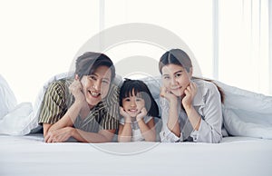 Happy asian young family spend time together. Dad mom daughter are smiling lying on the bed