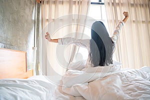 Happy Asian Young Girl Greets New Day with Warm Sunlight Flare, Sun shines on her from the big window