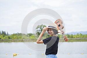 Happy asian young girl wera hat black shirt and jean with ukulele at park