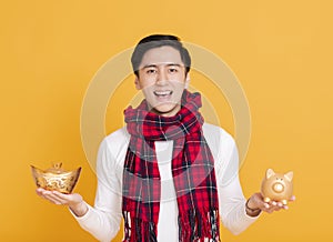 Happy asian young man showing chinese gold ingot and piggy bank
