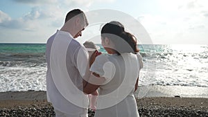 Happy Asian young mother kissing hand of baby daughter as father holding child in hands at sunset. Happy interracial