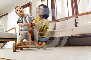 Happy Asian Young Mother playing with her little son at home, Little toddler boy having fun ride on rocking horse