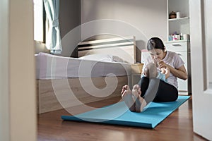 Happy Asian young mother in playing and holding and kissing her newborn or infant baby feet while practicing yoga in bedroom