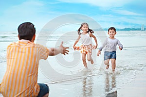 Happy asian young single dad playing with his children boy and girl, they running on sandy beach during sunny day with laughing