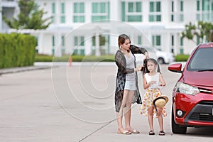 Happy asian young single mom, long hair dress up and combed her daughter with red car beside