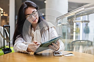 Happy Asian young woman sitting at cafe with coffee cup taking notes enjoying break