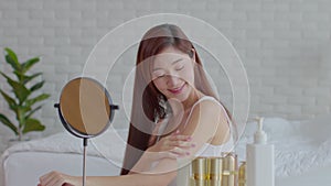 Happy Asian young woman smile and looking in mirror doing skin care applying lotion on her shoulder and beauty treatment at home,