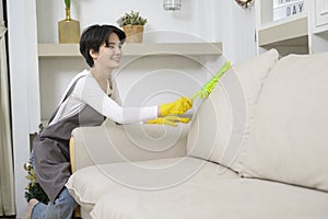 Happy Asian young woman sweeping sofa and furniture to cleaning house, healthy lifestyle concept